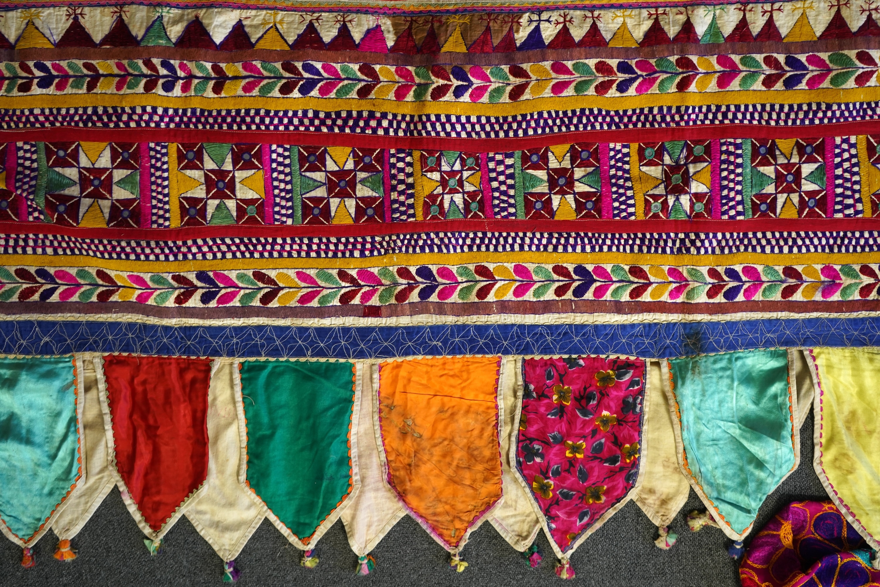 A large Indian silk embroidered and mirrored temple pelmet, with a cerise silk embroidered hanging and a length of cotton wax resist style printed fabric. Temple pelmet 468cm long x 70cm, deep. Condition - the pelmet has